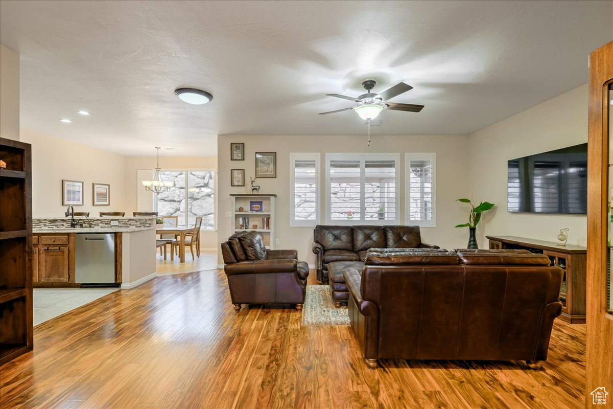 Living room with ceiling fan with notable chandelier and light hardwood / wood-style flooring