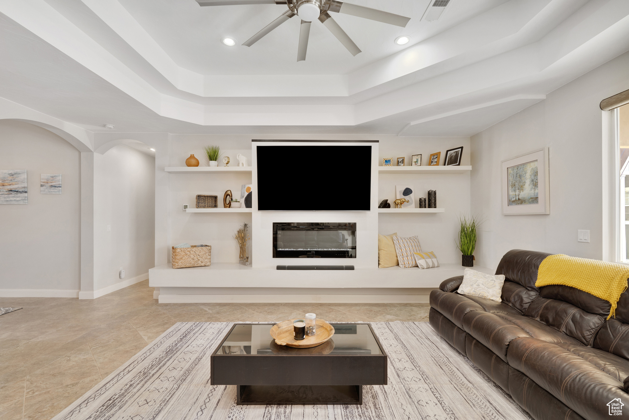 Living room featuring built in shelves, a tray ceiling, and ceiling fan