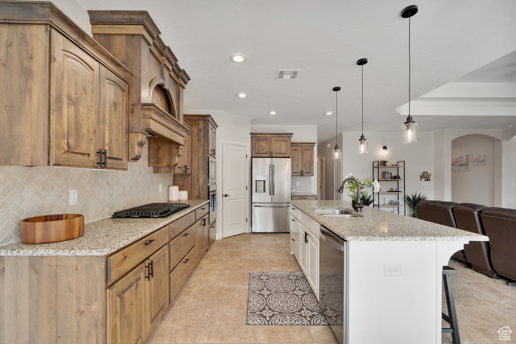 Kitchen with sink, light stone countertops, tasteful backsplash, decorative light fixtures, and stainless steel appliances