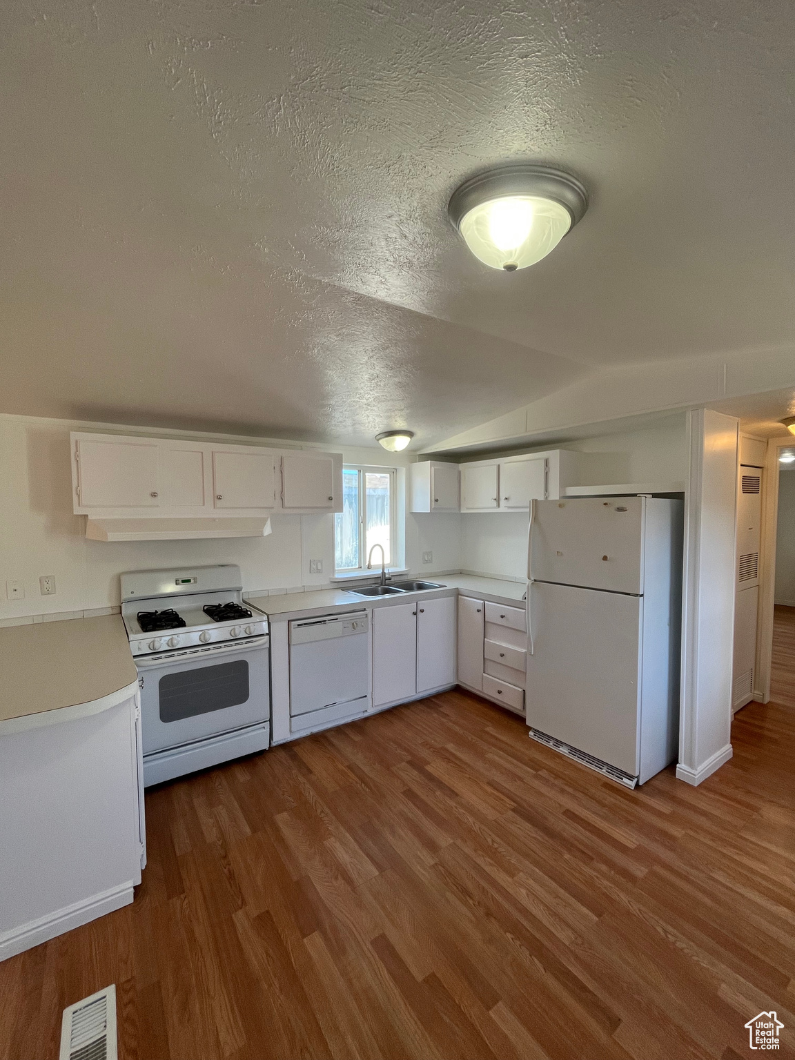 Kitchen featuring sink, white cabinets, wood-type flooring, and white appliances