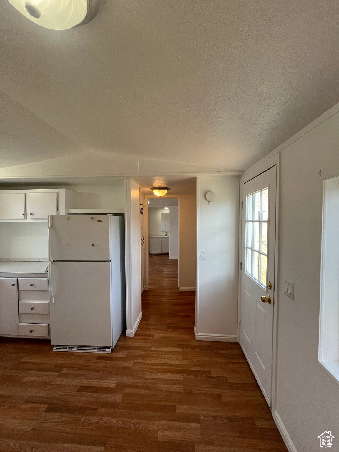 Kitchen with dark hardwood / wood-style floors, white refrigerator, white cabinetry, and a textured ceiling