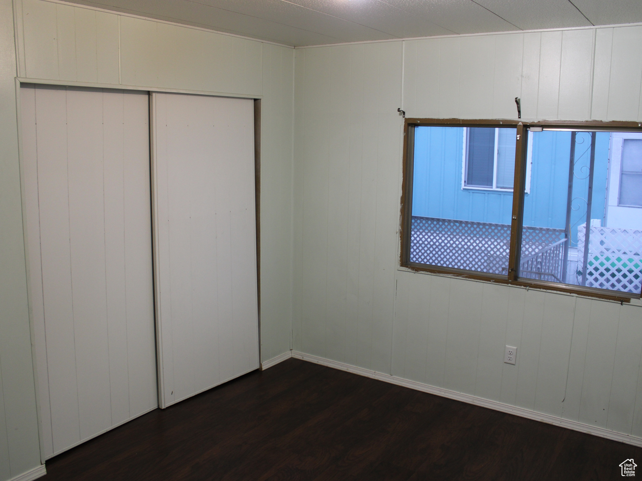 Unfurnished bedroom featuring dark hardwood / wood-style floors, a closet, and wooden walls