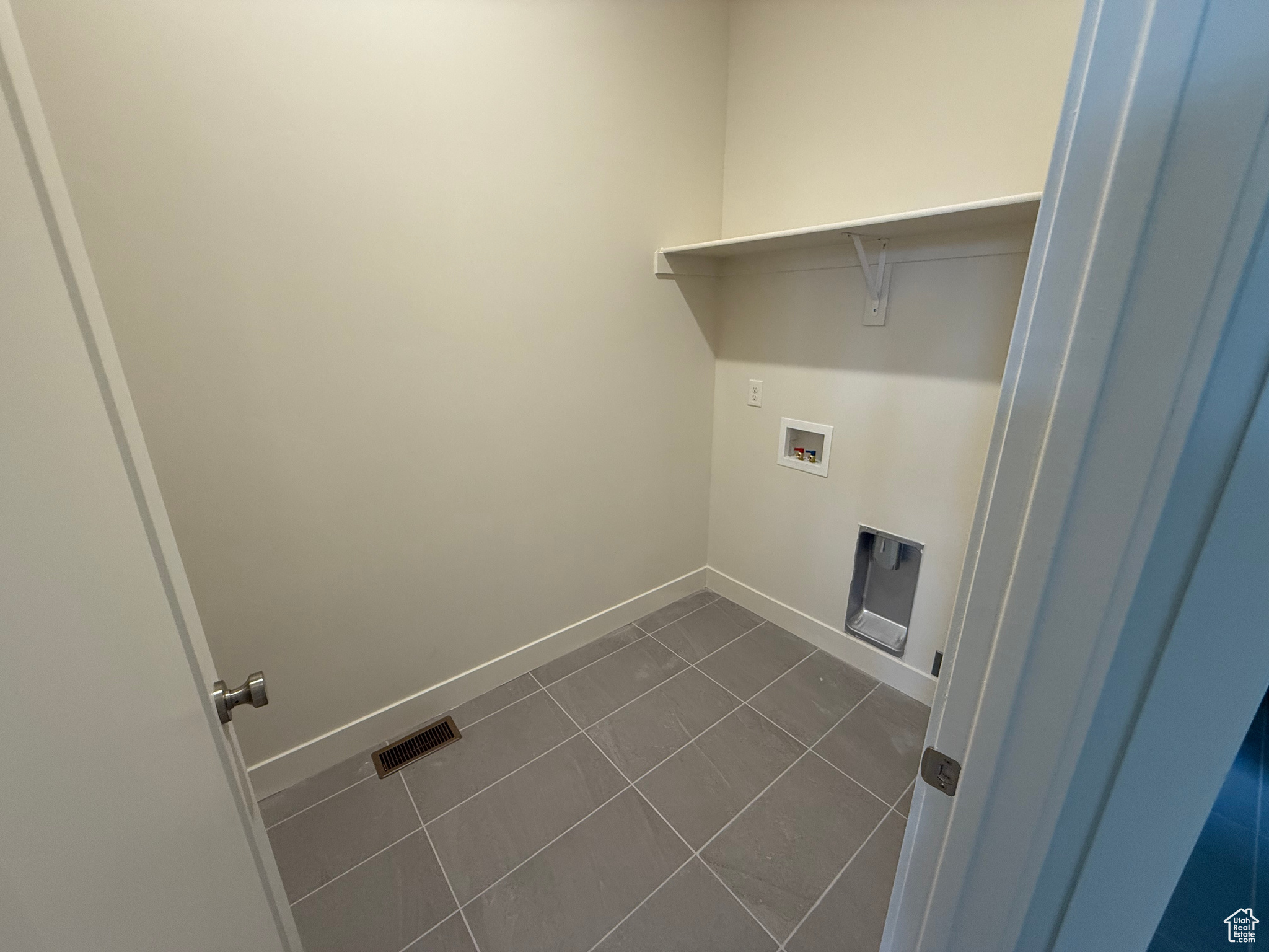 Clothes washing area with washer hookup and dark tile patterned floors.