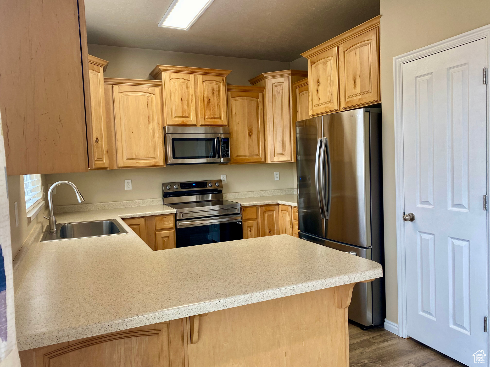 Kitchen featuring kitchen peninsula, sink, light brown cabinets, and appliances with stainless steel finishes