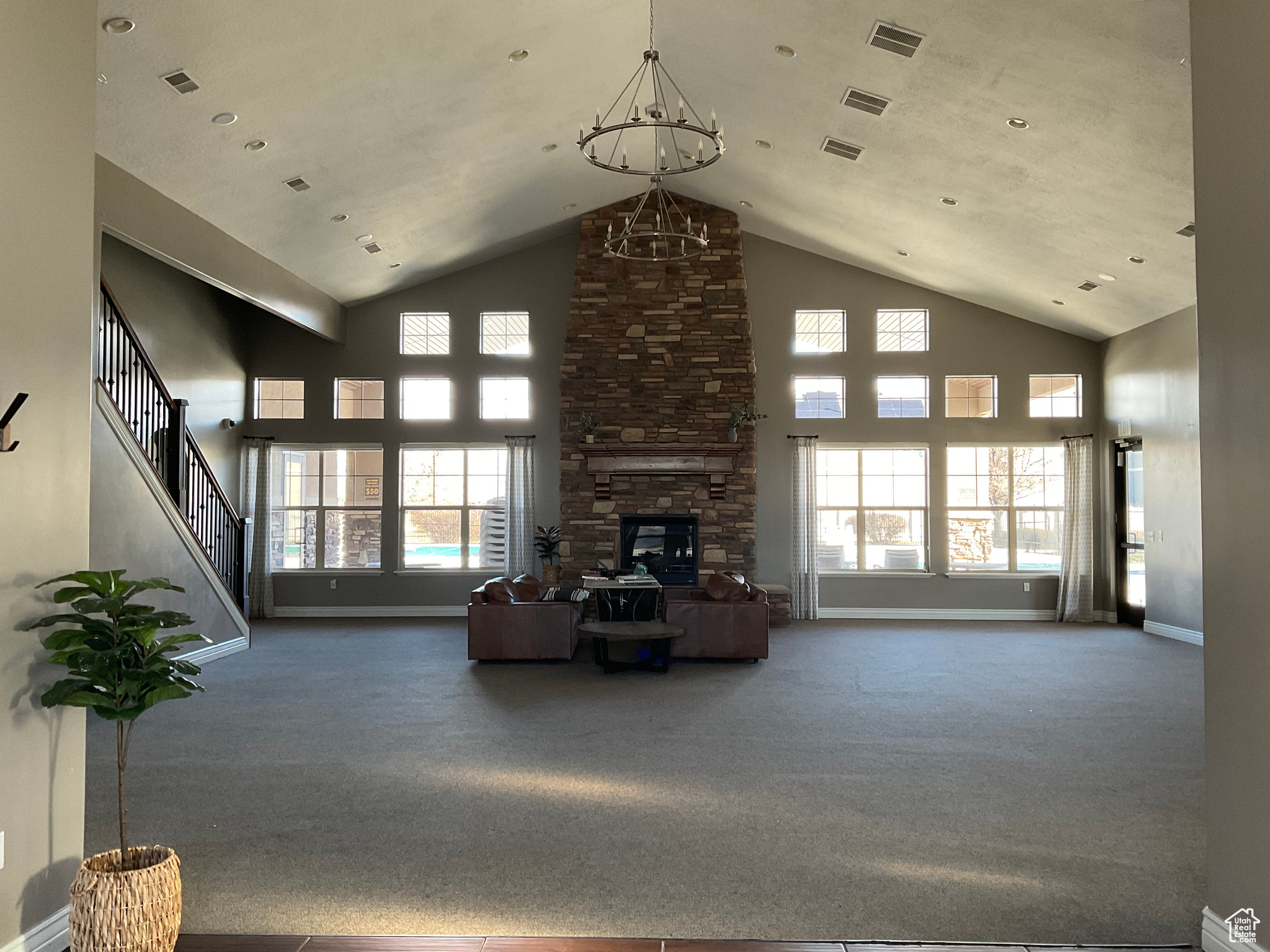 Unfurnished living room with carpet flooring, an inviting chandelier, a wealth of natural light, and a stone fireplace