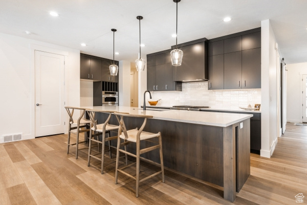 Kitchen with pendant lighting, wall chimney exhaust hood, light wood-type flooring, and sink