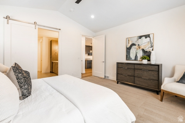 Carpeted bedroom with ensuite bath, vaulted ceiling, and a barn door