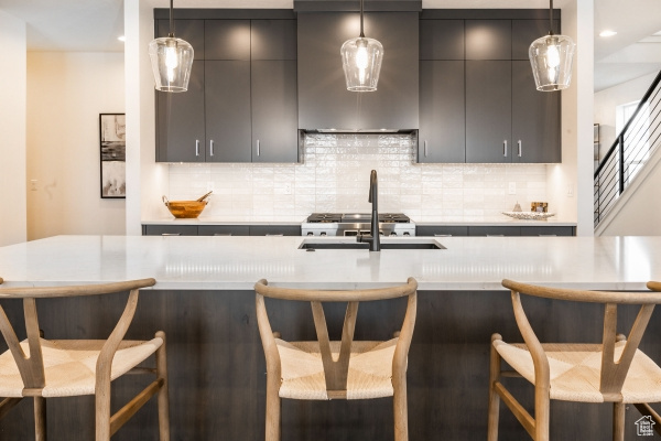 Kitchen with sink, wall chimney exhaust hood, a kitchen breakfast bar, pendant lighting, and decorative backsplash