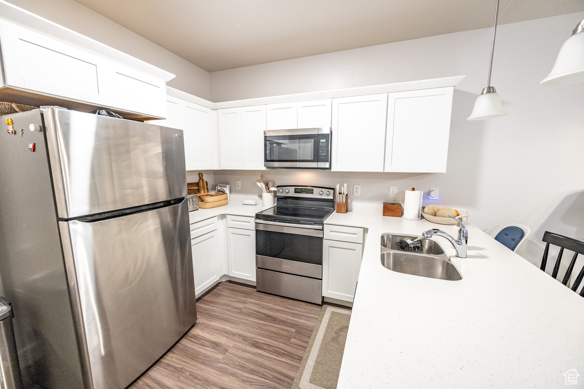 Kitchen featuring appliances with stainless steel finishes, sink, light hardwood / wood-style flooring, white cabinetry, and hanging light fixtures