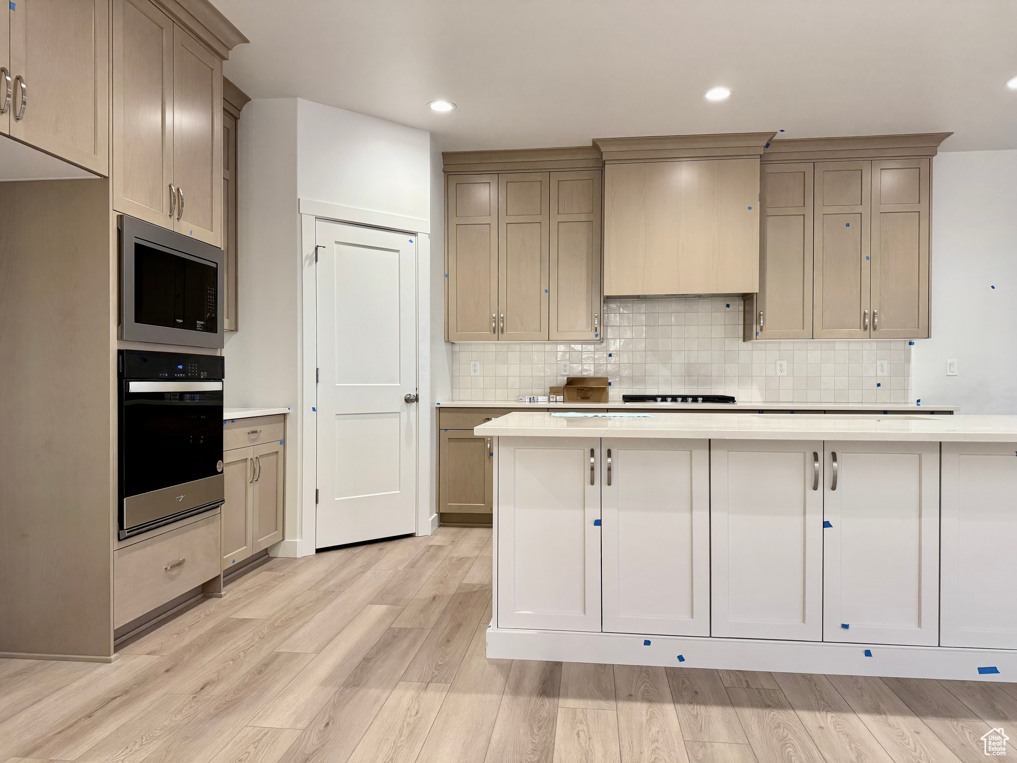 Kitchen featuring backsplash, light hardwood / wood-style floors, premium range hood, and appliances with stainless steel finishes