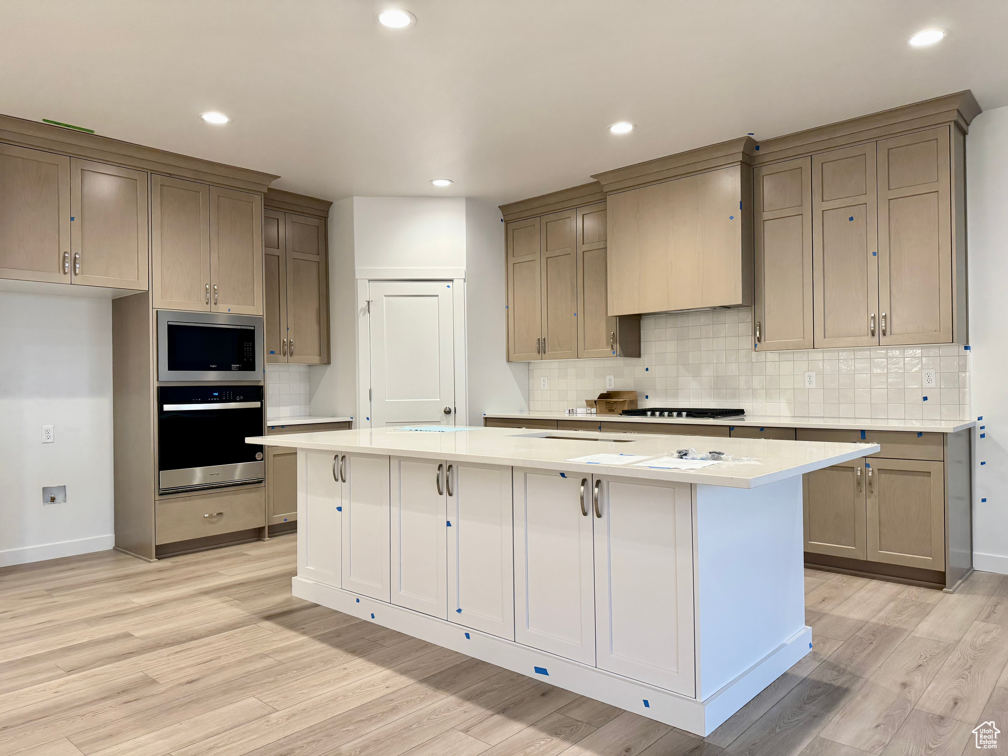 Kitchen with light wood-type flooring, appliances with stainless steel finishes, a center island, and premium range hood