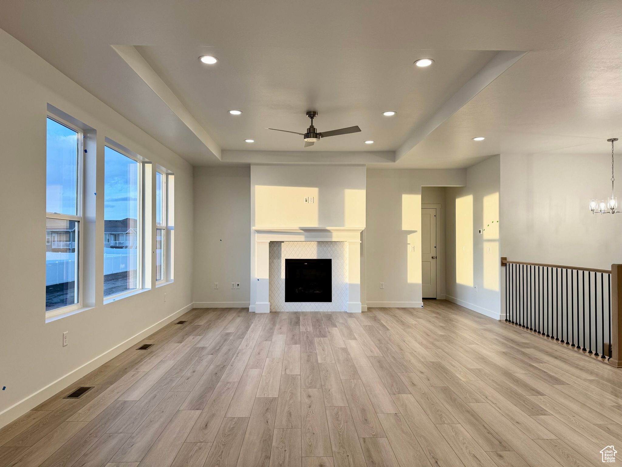 Unfurnished living room featuring a fireplace, light wood-type flooring, a raised ceiling, and ceiling fan with notable chandelier