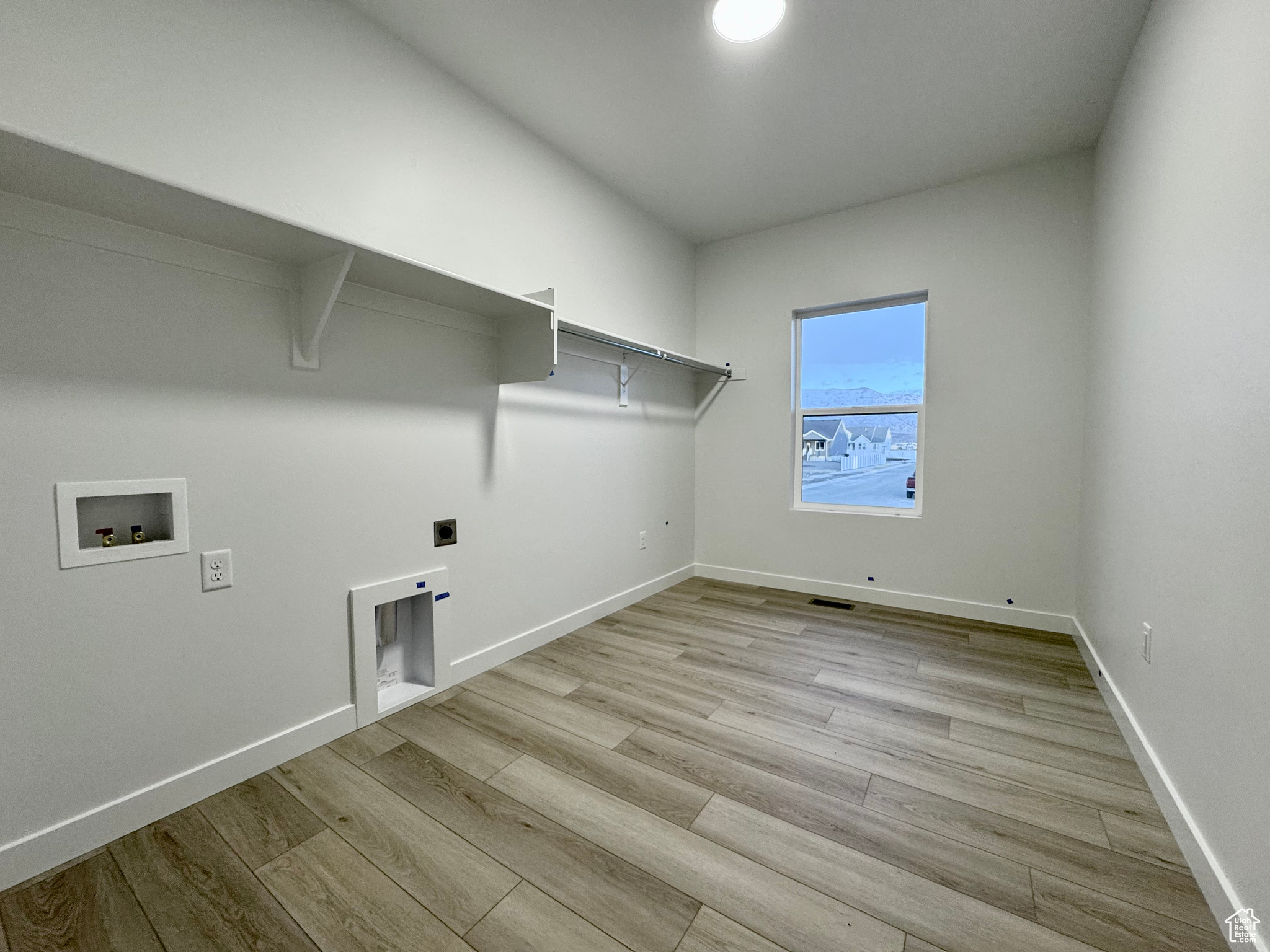 Clothes washing area with hookup for an electric dryer, hookup for a washing machine, and light hardwood / wood-style flooring