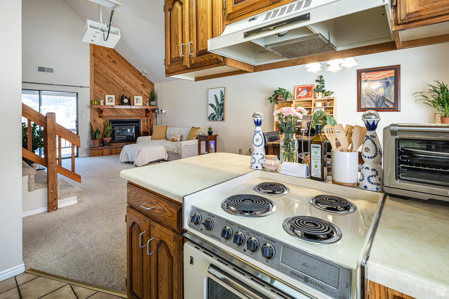 Kitchen featuring a large fireplace, white electric stove, wood walls, light colored carpet, and lofted ceiling