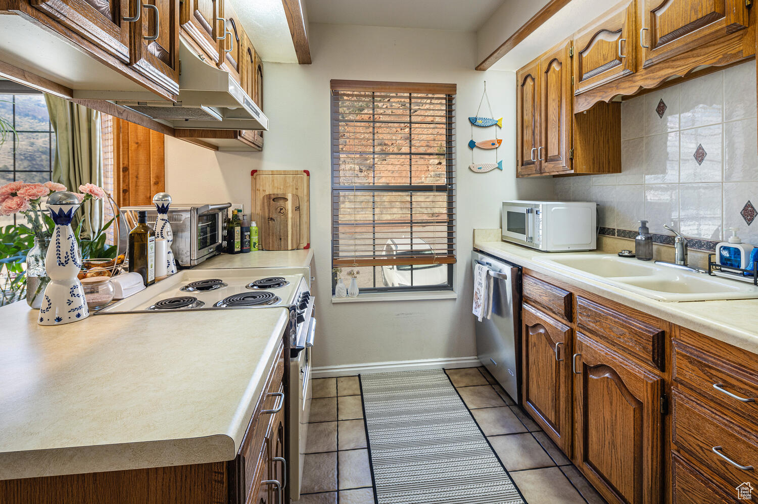 Kitchen featuring decorative backsplash, white appliances, sink, and light tile patterned floors