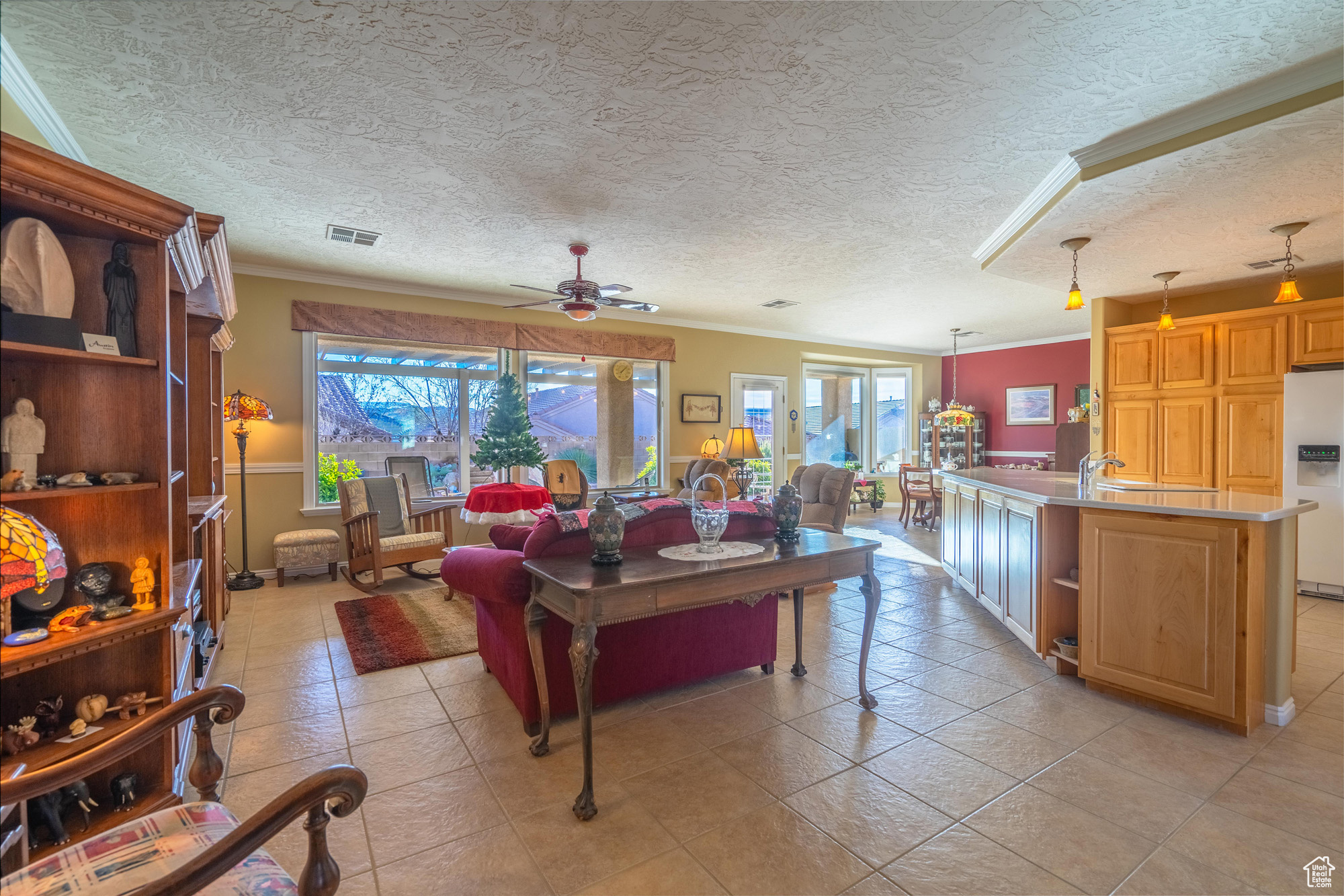 Great room with light tile patterned floors, a textured ceiling, ceiling fan, and ornamental molding