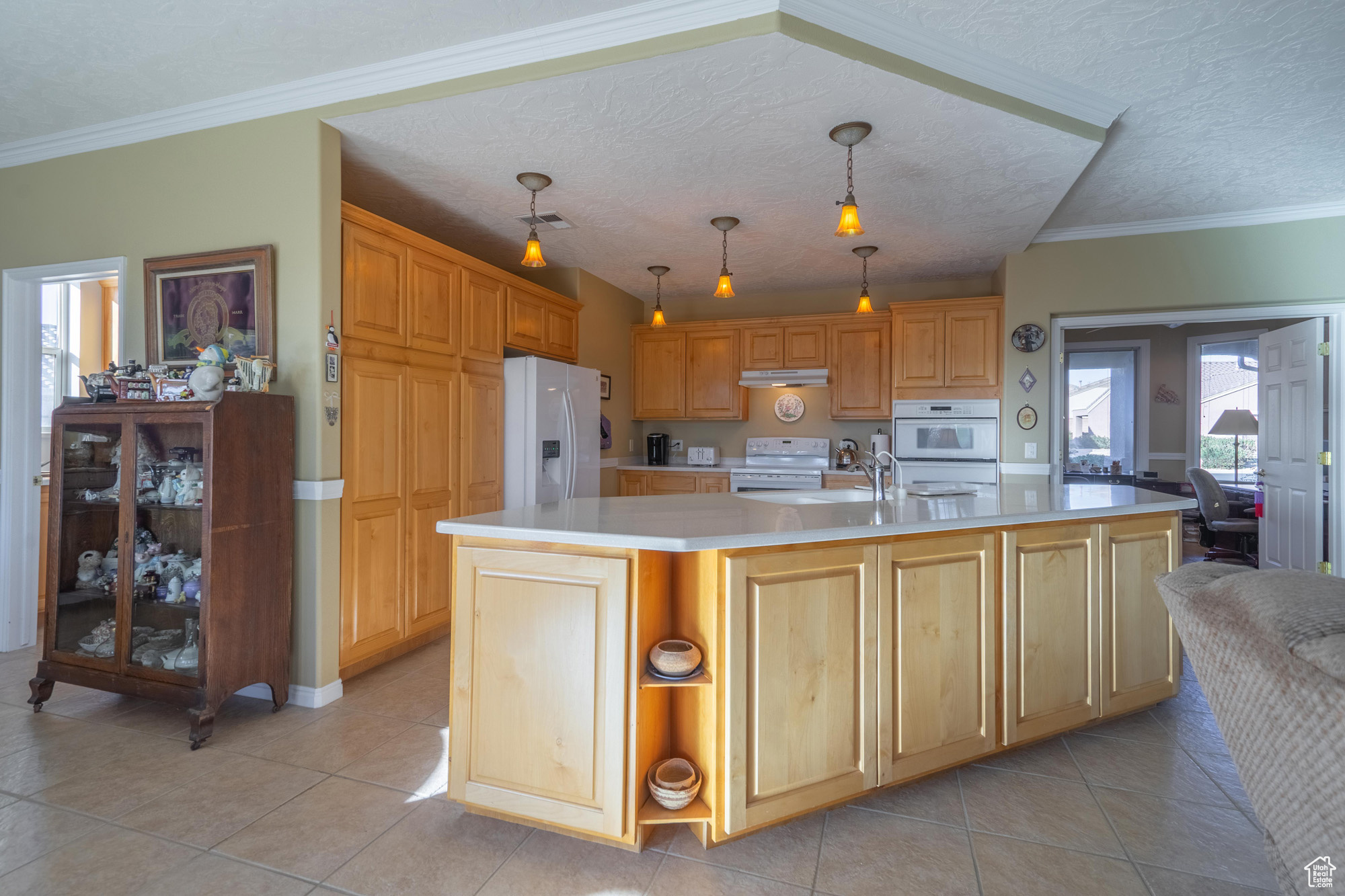 Kitchen featuring a center island with sink, white appliances, hanging light fixtures, and a textured ceiling