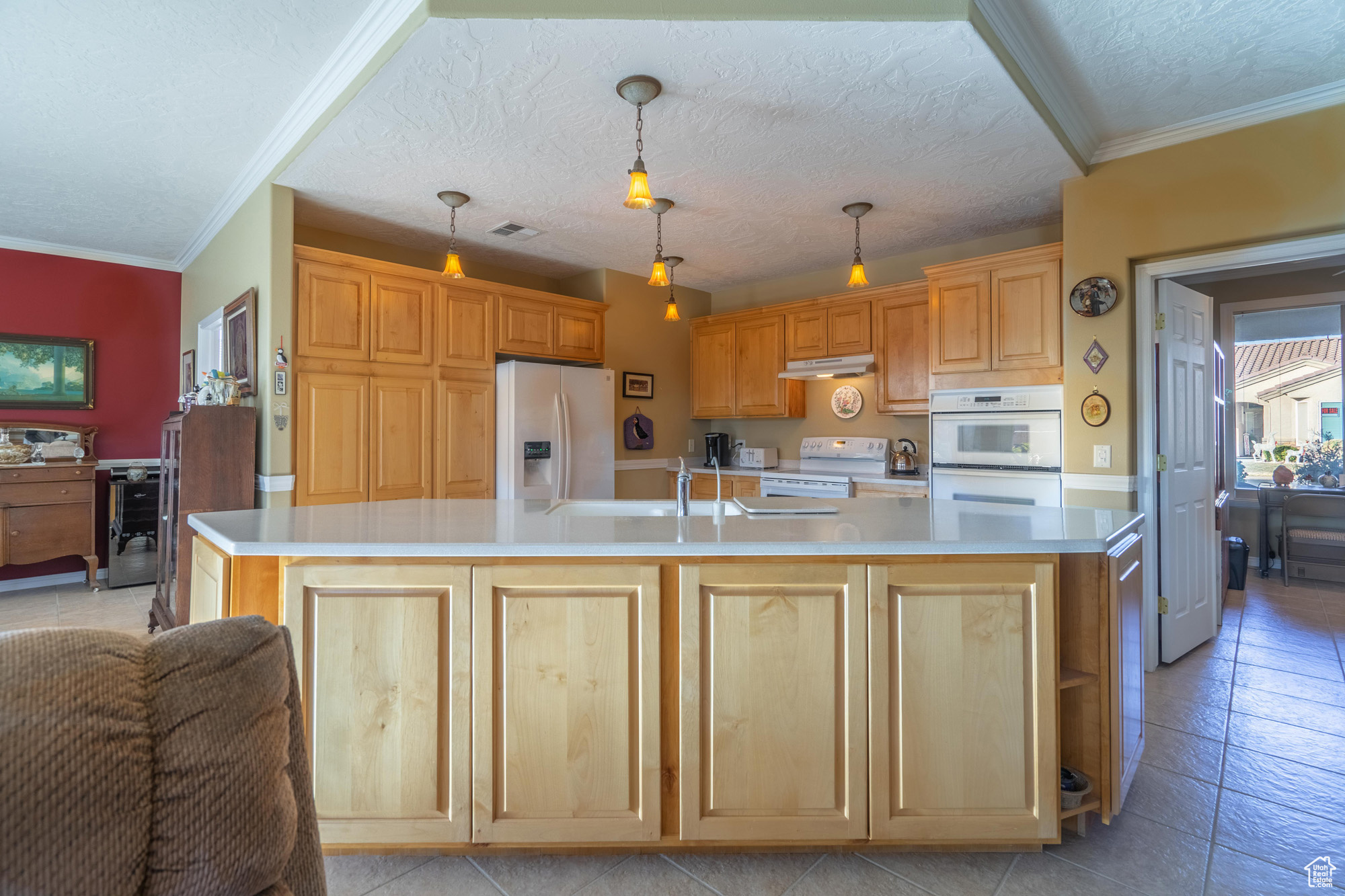 Kitchen with white appliances, decorative light fixtures, a kitchen island with sink, and extra cabinets on front