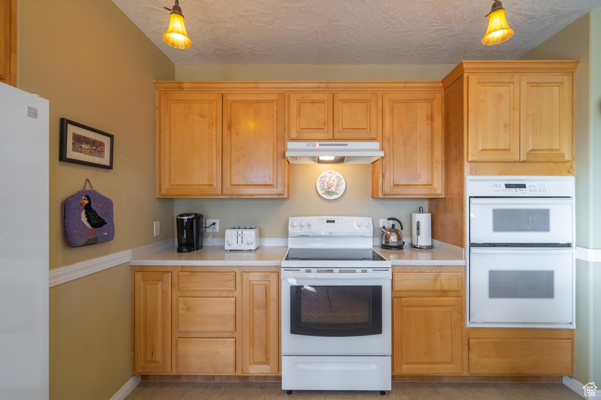 Kitchen featuring decorative light fixtures, white appliances, a textured ceiling, and light tile patterned floors