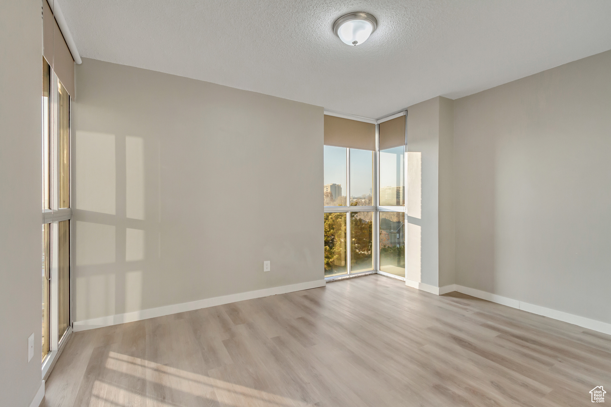 Unfurnished room with light hardwood / wood-style flooring, expansive windows, and a textured ceiling