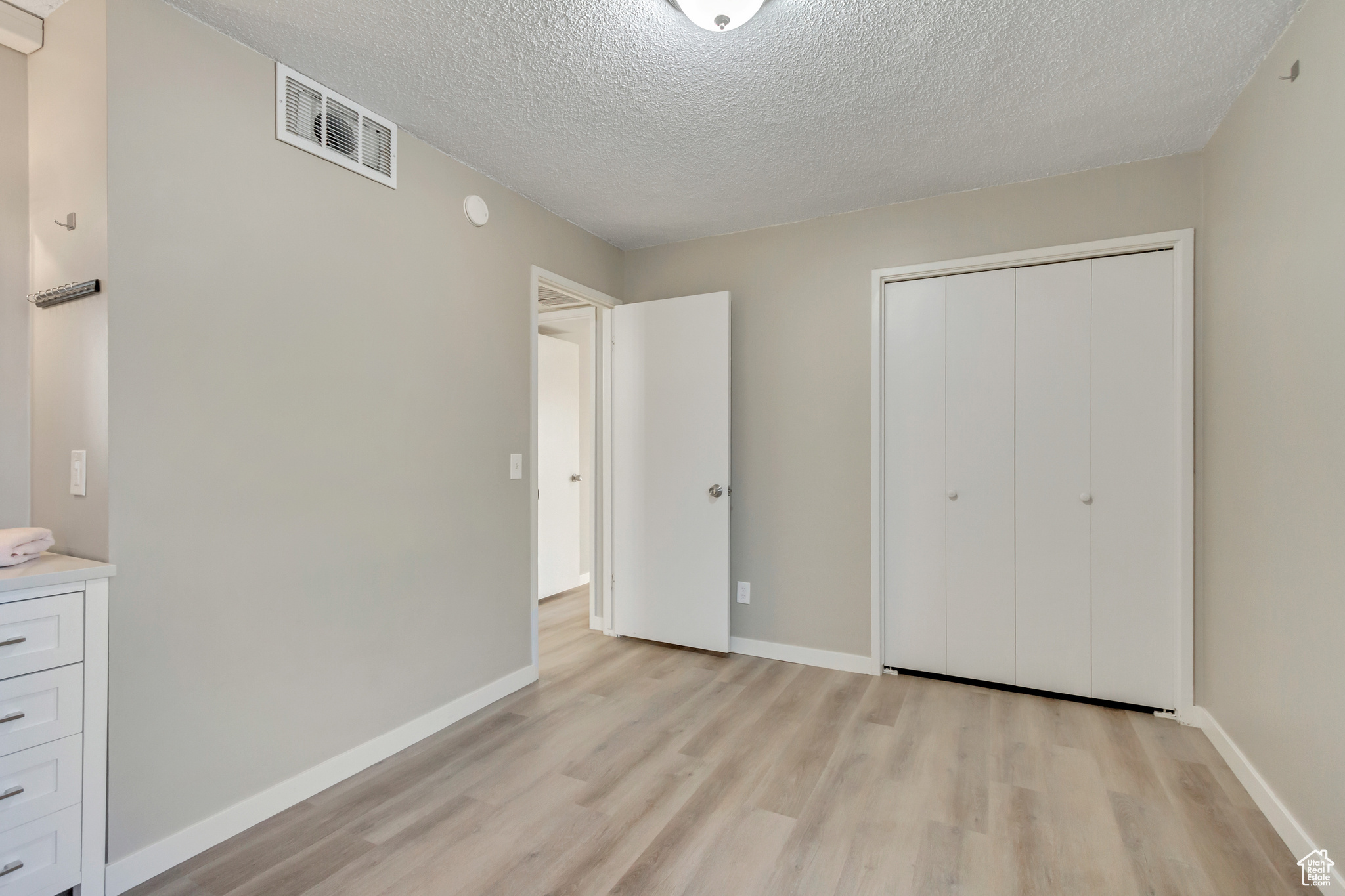 Unfurnished bedroom featuring a closet, a textured ceiling, and light hardwood / wood-style flooring