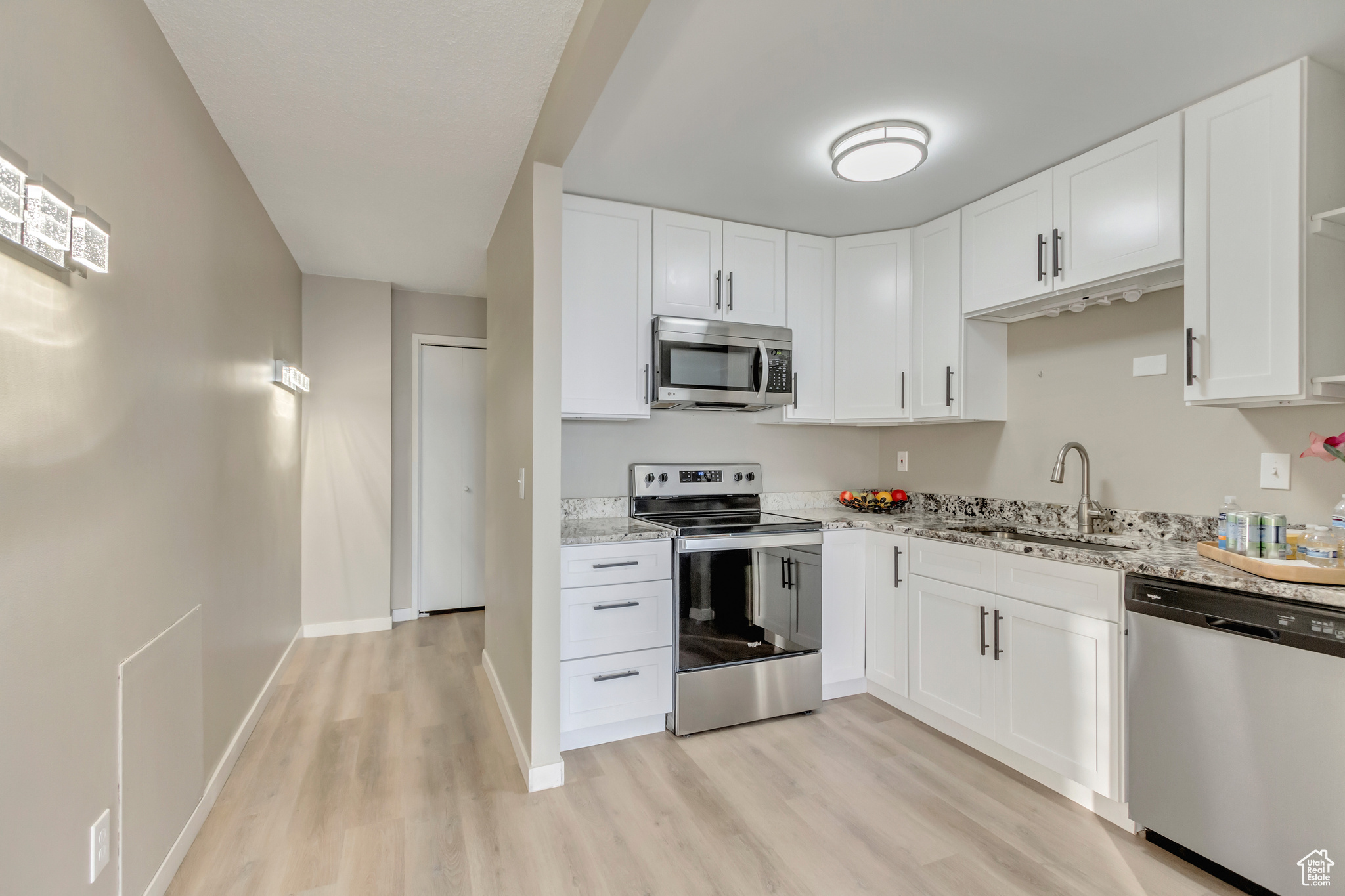 Kitchen with sink, light stone countertops, appliances with stainless steel finishes, light hardwood / wood-style floors, and white cabinetry