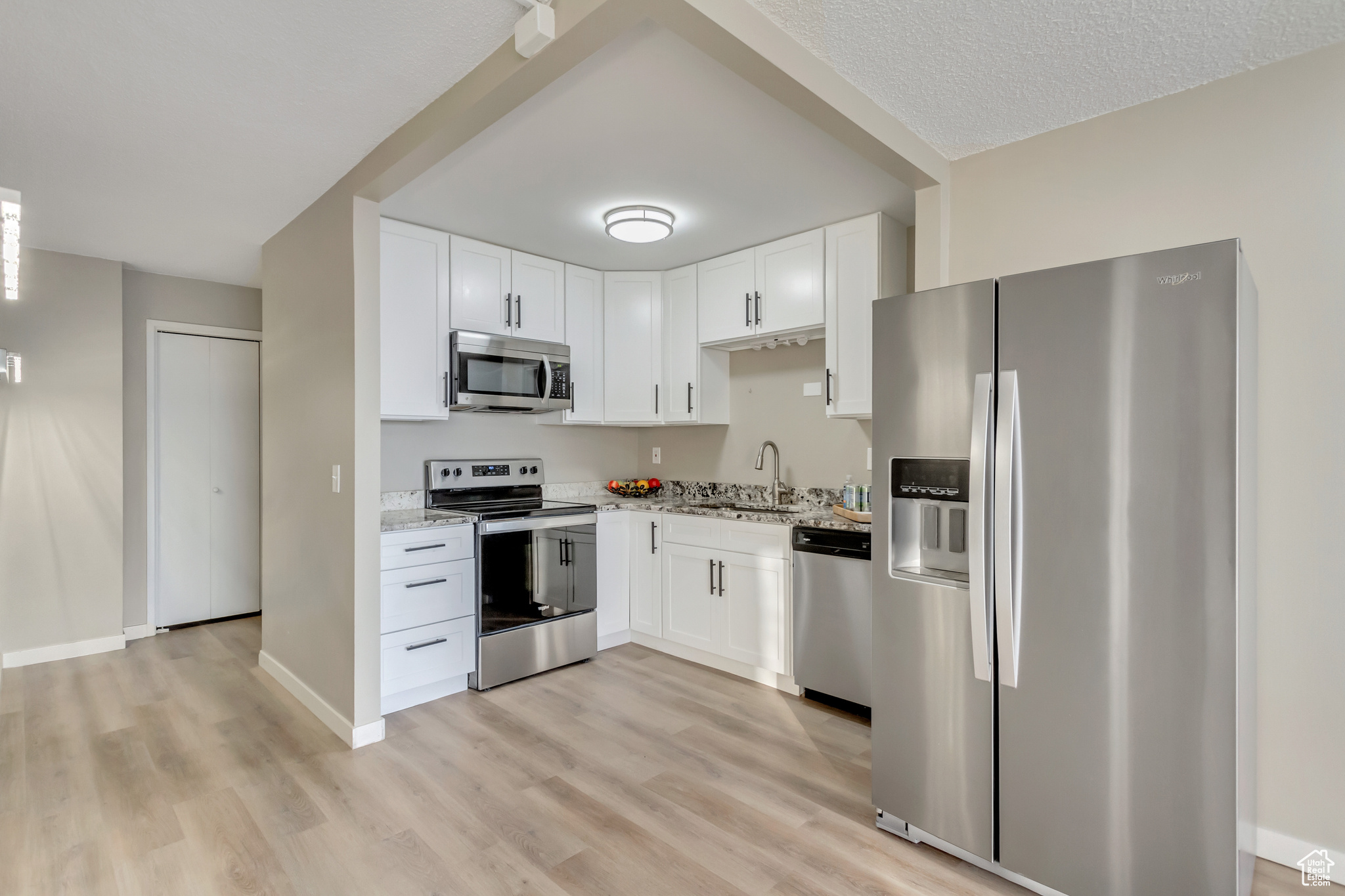 Kitchen featuring light stone countertops, sink, white cabinets, and appliances with stainless steel finishes