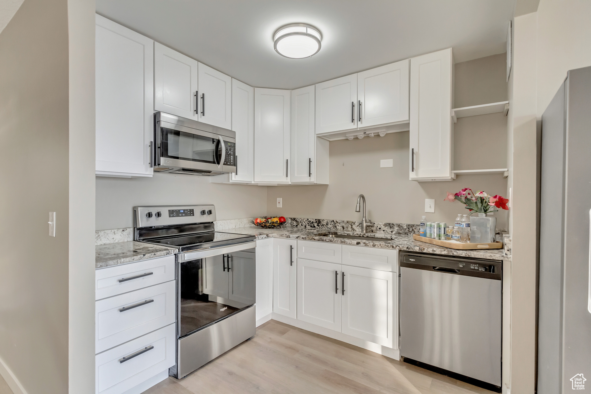 Kitchen featuring light stone counters, stainless steel appliances, sink, light hardwood / wood-style flooring, and white cabinetry