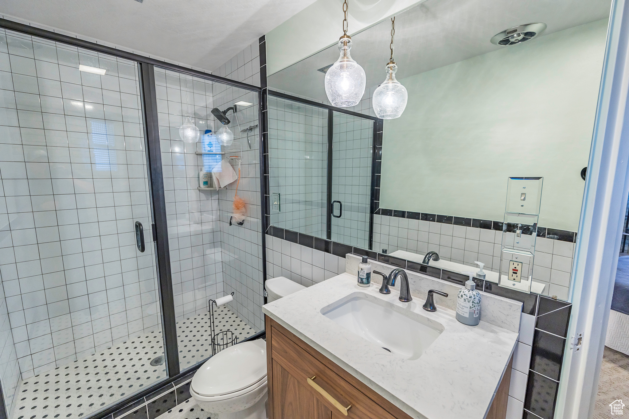 Bathroom featuring vanity, toilet, a shower with shower door, and tile walls