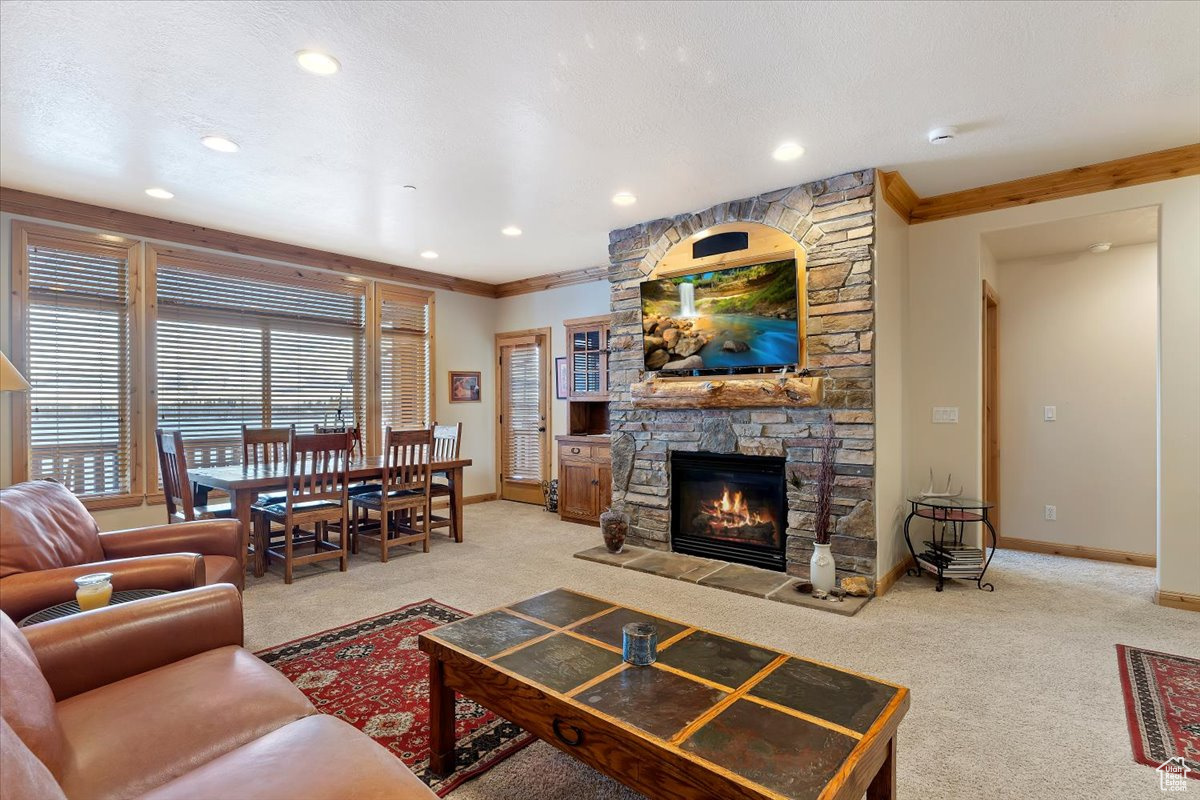 Main level Living room featuring carpet, a stone fireplace, and crown molding