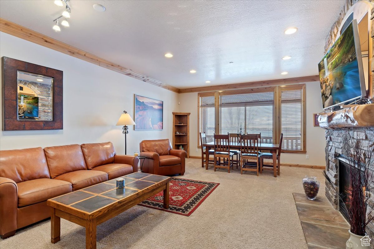 Carpeted living room with a stone fireplace, ornamental molding, a textured ceiling, can lighting.