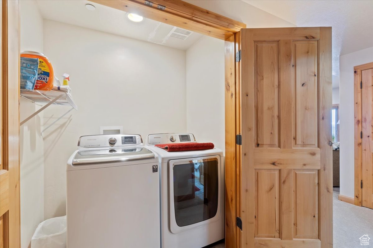 Washroom with light colored carpet and washer and dryer