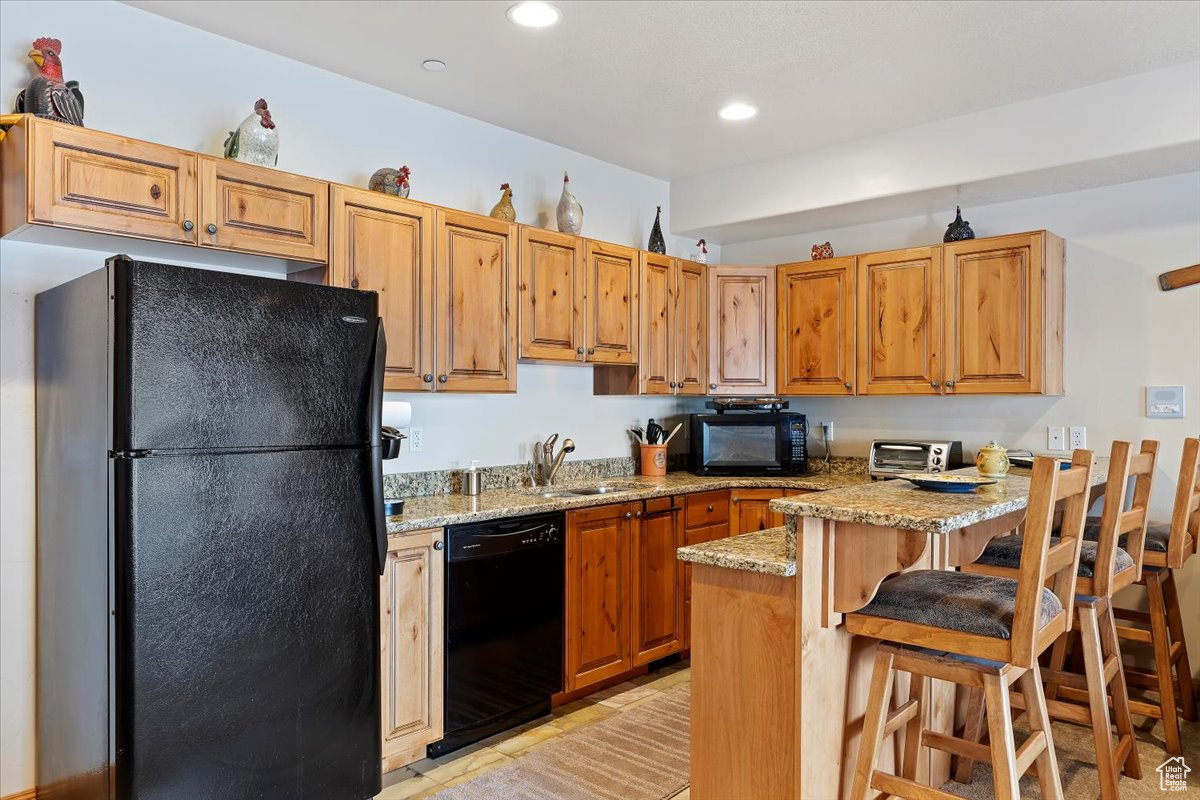 Kitchen featuring kitchen peninsula, a kitchen breakfast bar, light stone counters, sink, and black appliances