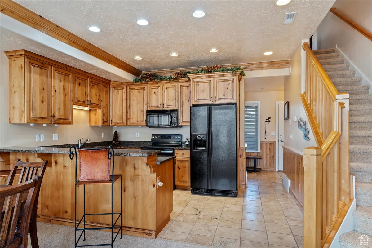 Kitchen with wood walls, black appliances, a kitchen breakfast bar, dark stone countertops, and kitchen peninsula