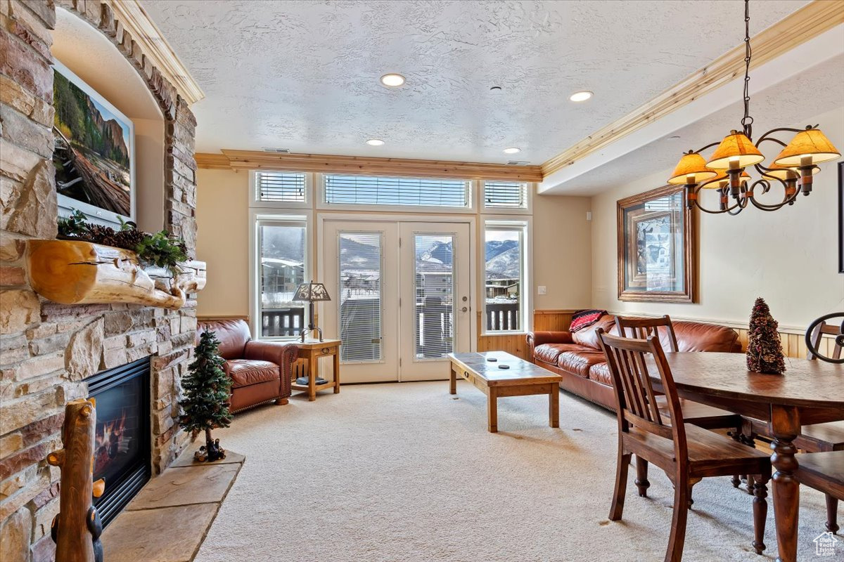 Dining area featuring carpet flooring, ornamental molding, a textured ceiling, a chandelier, and a stone gas  fireplace