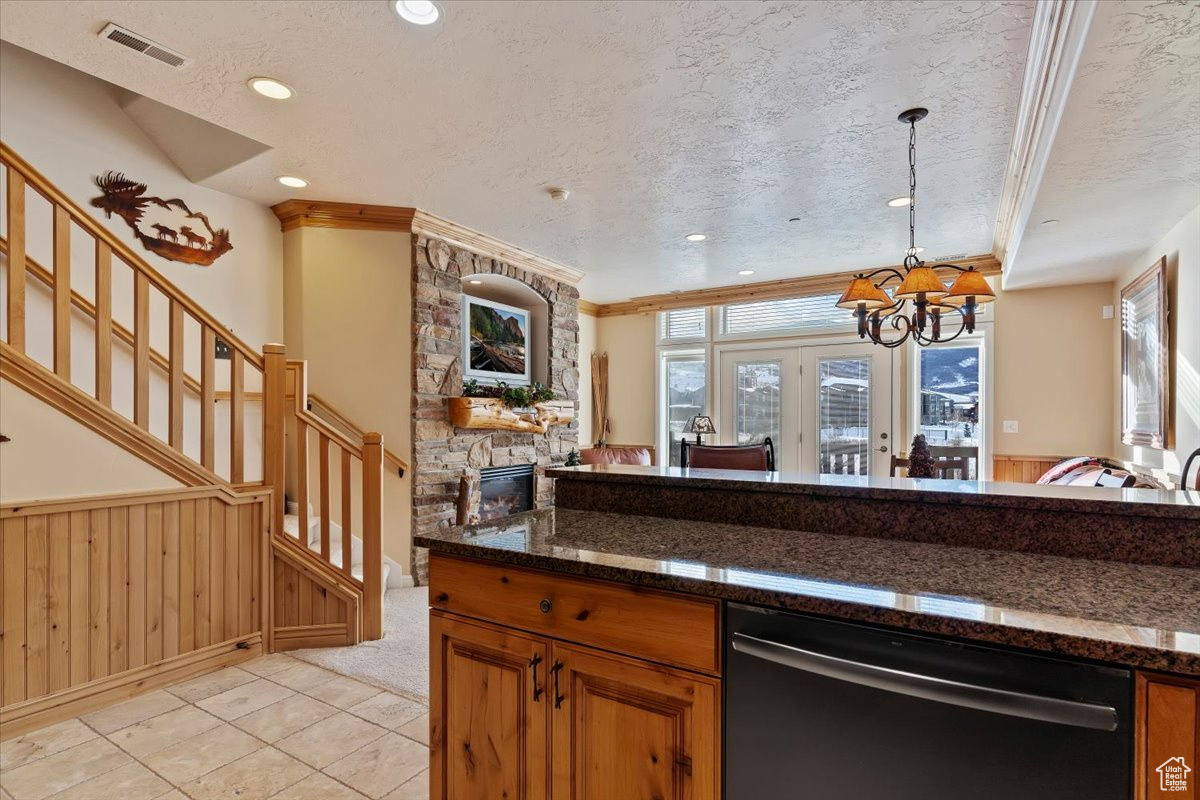 Kitchen featuring granite counters, a textured ceiling, dishwasher, a stone fireplace, and hanging light fixtures