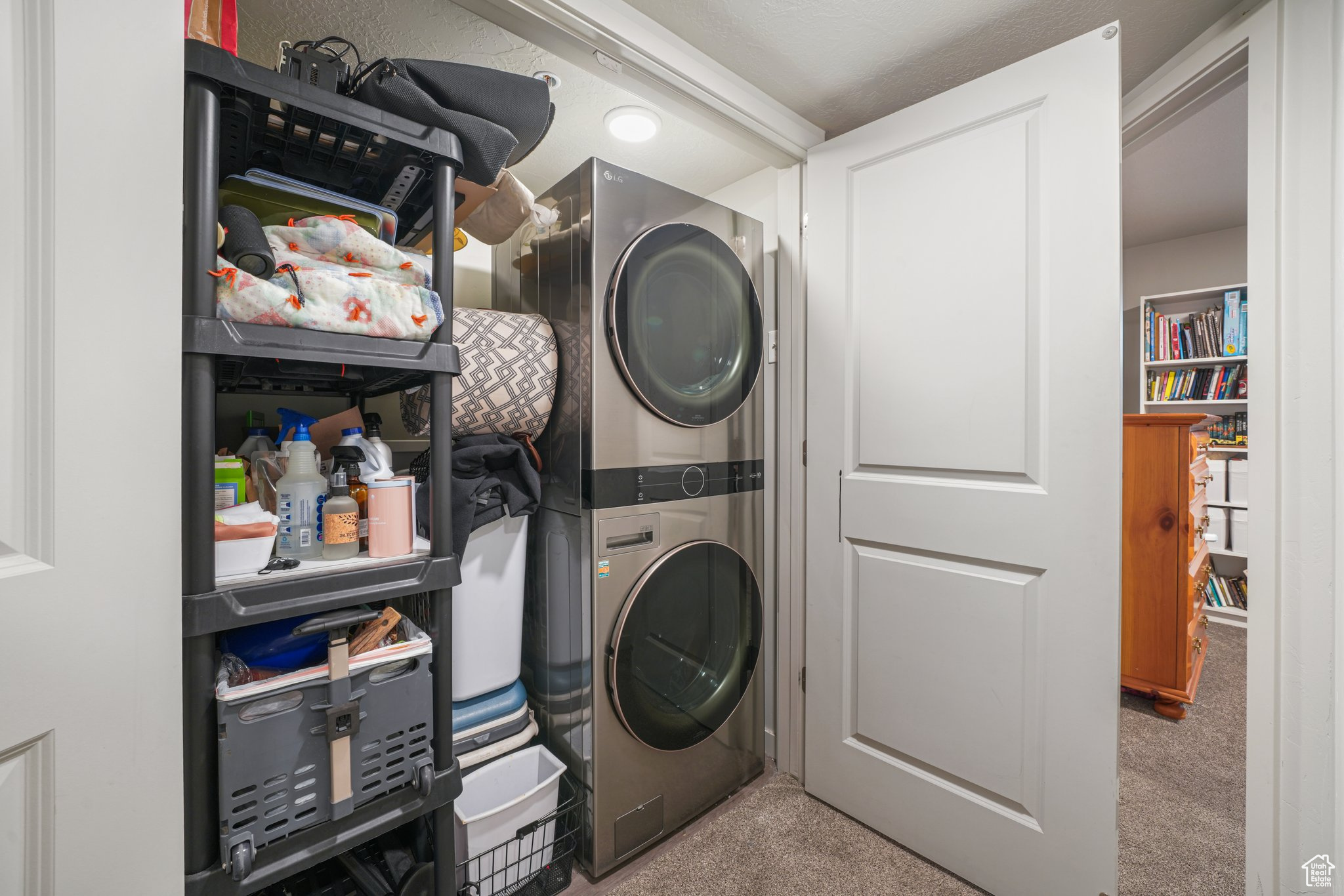 Laundry area featuring light colored carpet and stacked washer and clothes dryer