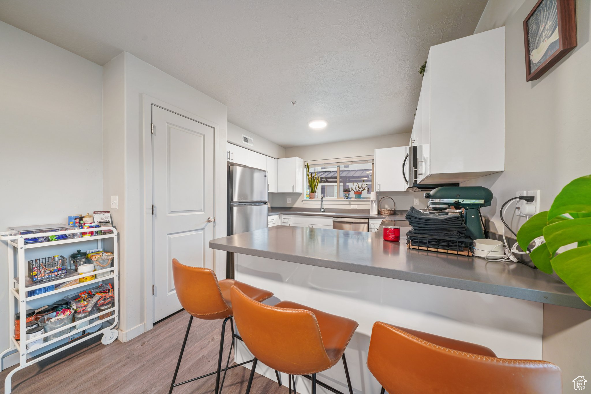 Kitchen with kitchen peninsula, appliances with stainless steel finishes, light wood-type flooring, and white cabinetry