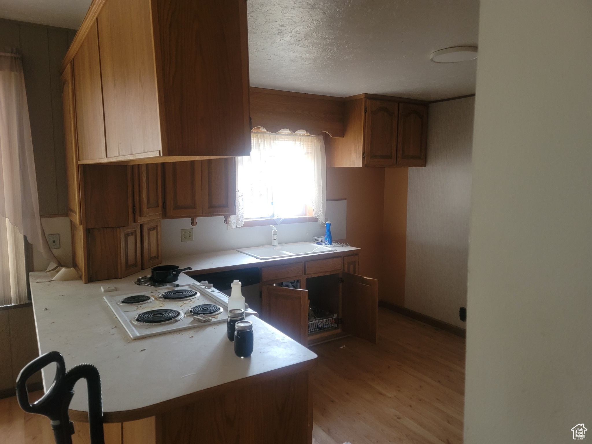 Kitchen with kitchen peninsula, light wood-type flooring, a textured ceiling, white stovetop, and sink