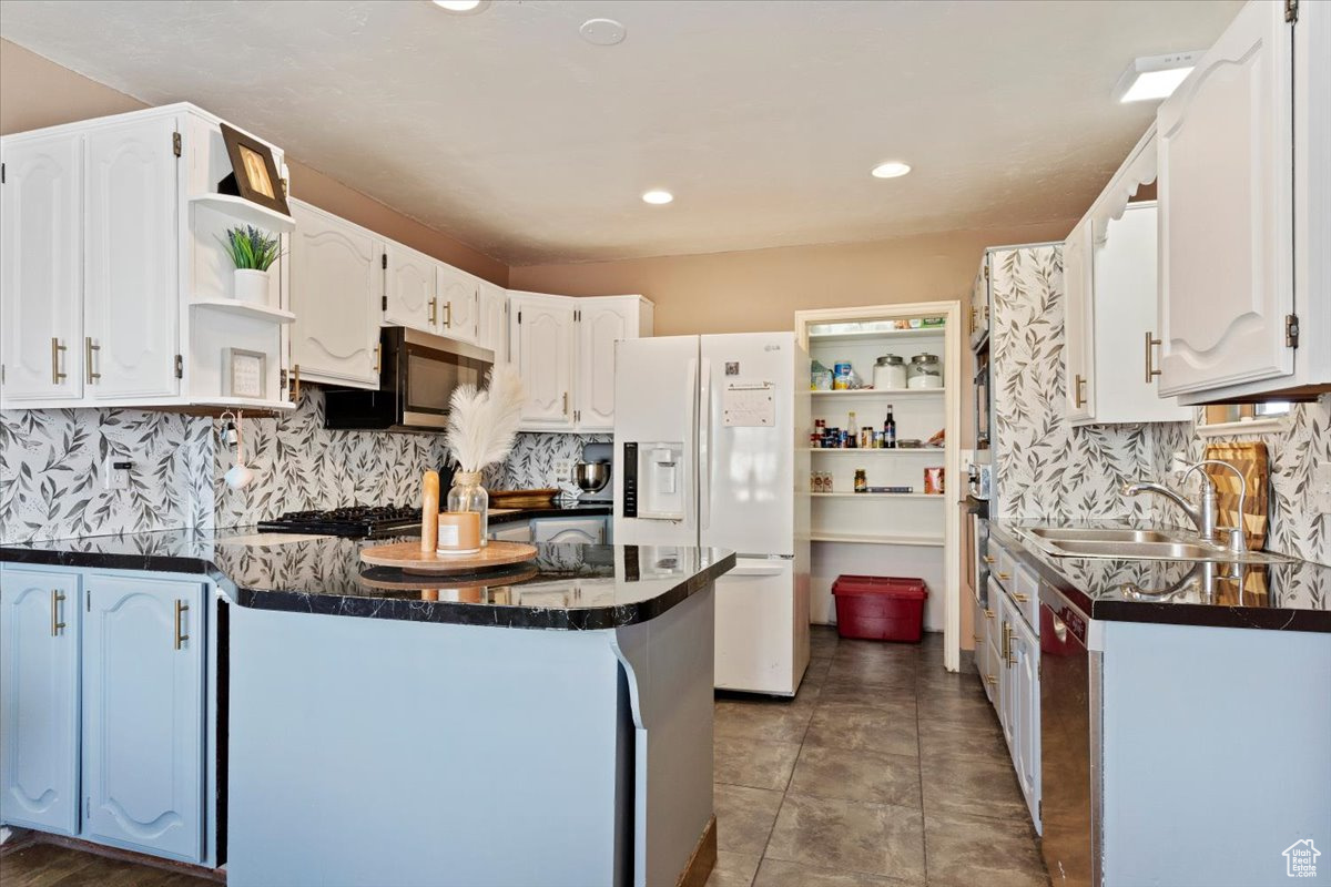 Kitchen with white refrigerator with ice dispenser, white cabinets, sink, tasteful backsplash, and kitchen peninsula