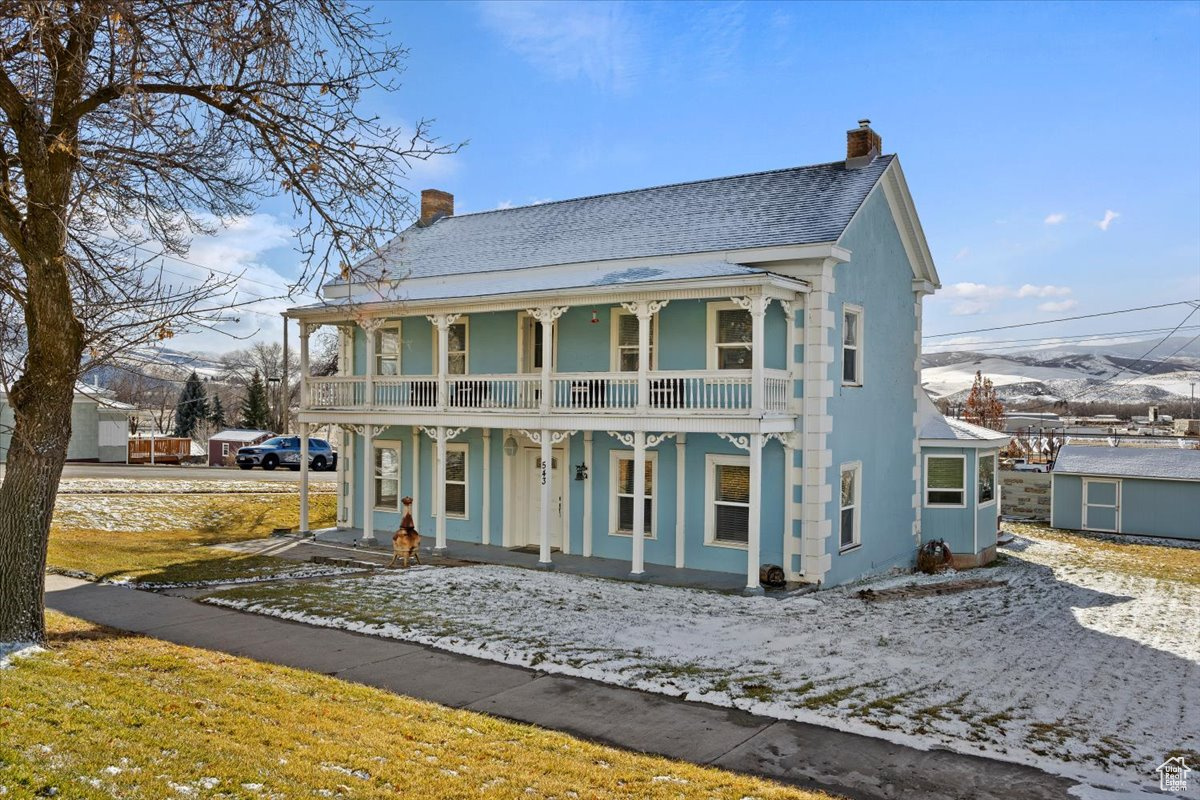 View of front of property with a mountain view, a porch, a balcony, and a shed