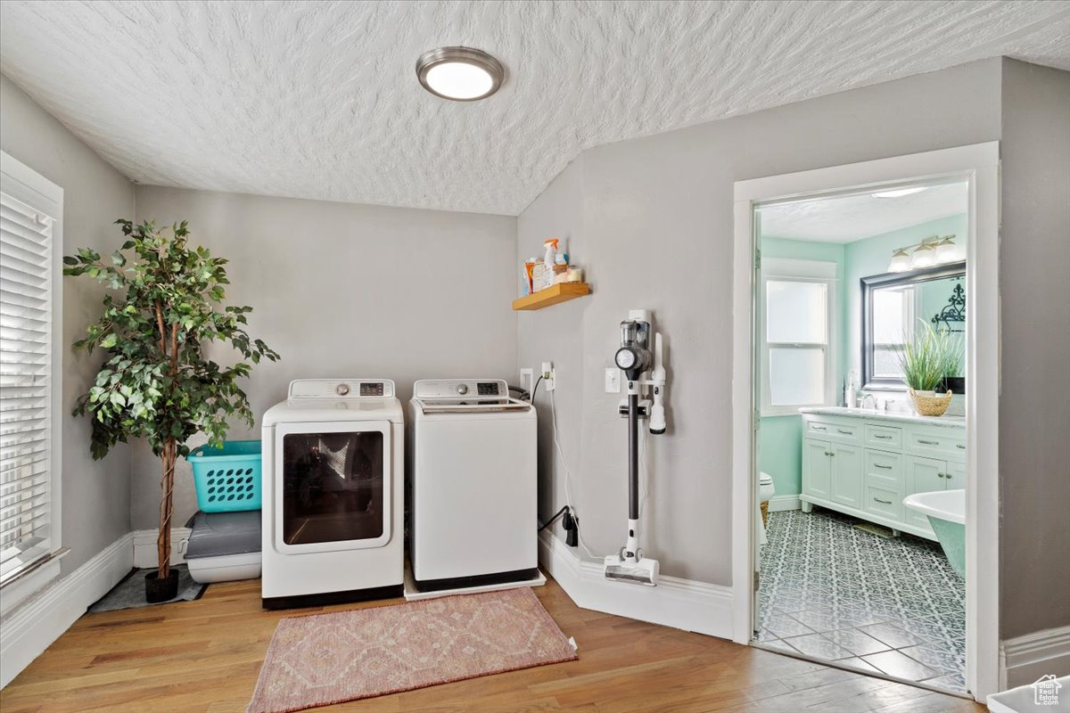 Laundry area featuring washer and clothes dryer, a textured ceiling, and light wood-type flooring