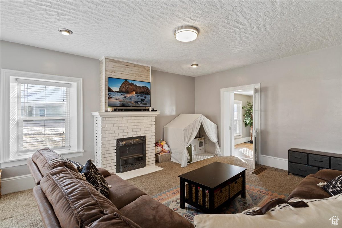 Living room featuring carpet flooring, a textured ceiling, and a brick fireplace