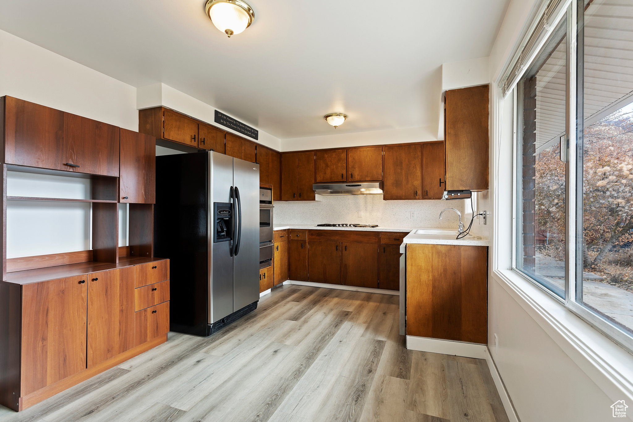 Kitchen with backsplash, light wood-type flooring, sink, and appliances with stainless steel finishes