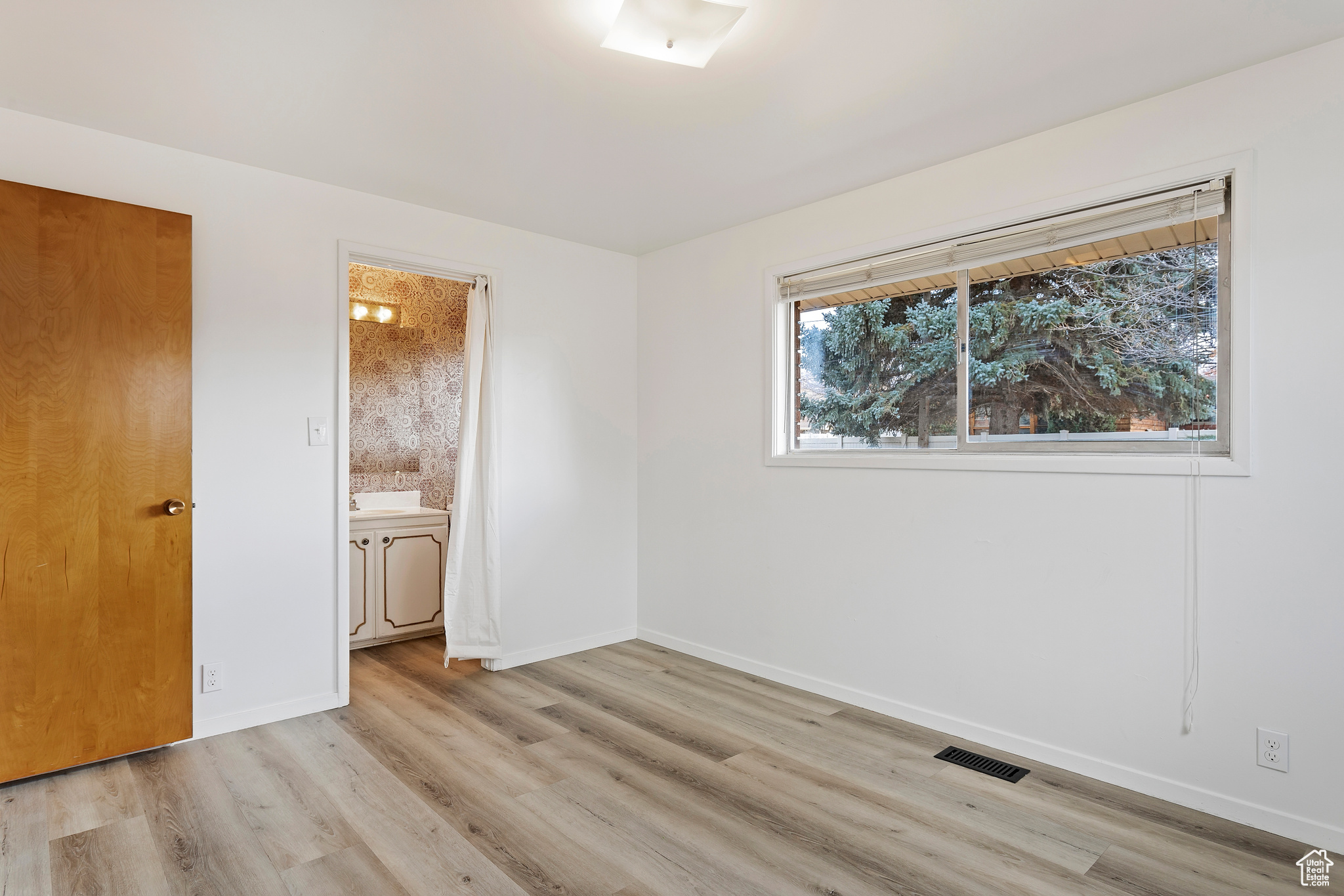 Unfurnished bedroom with connected bathroom and light wood-type flooring