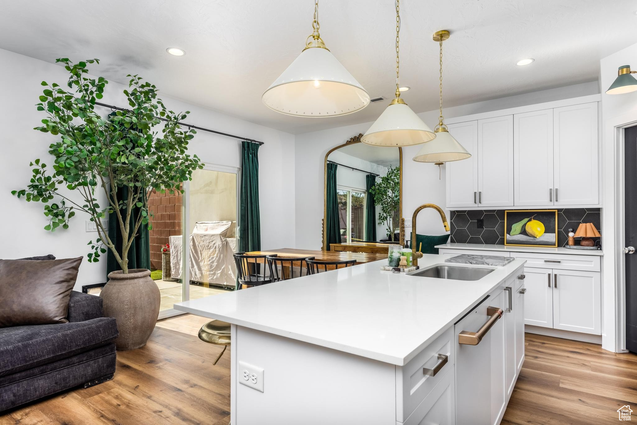 Open concept kitchen with decorative backsplash, sink, decorative light fixtures, a center island with sink, and white cabinets