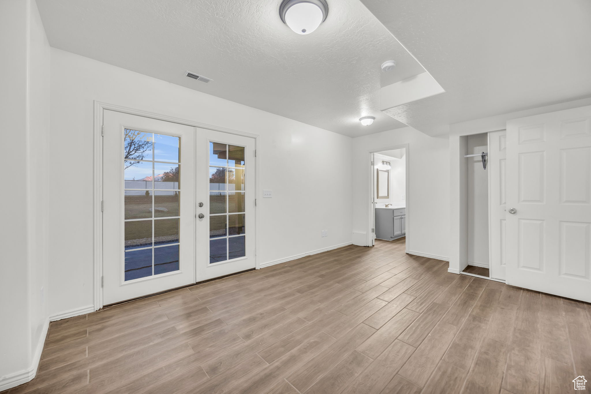 Unfurnished bedroom featuring access to exterior, french doors, light wood-type flooring, ensuite bath, and a textured ceiling