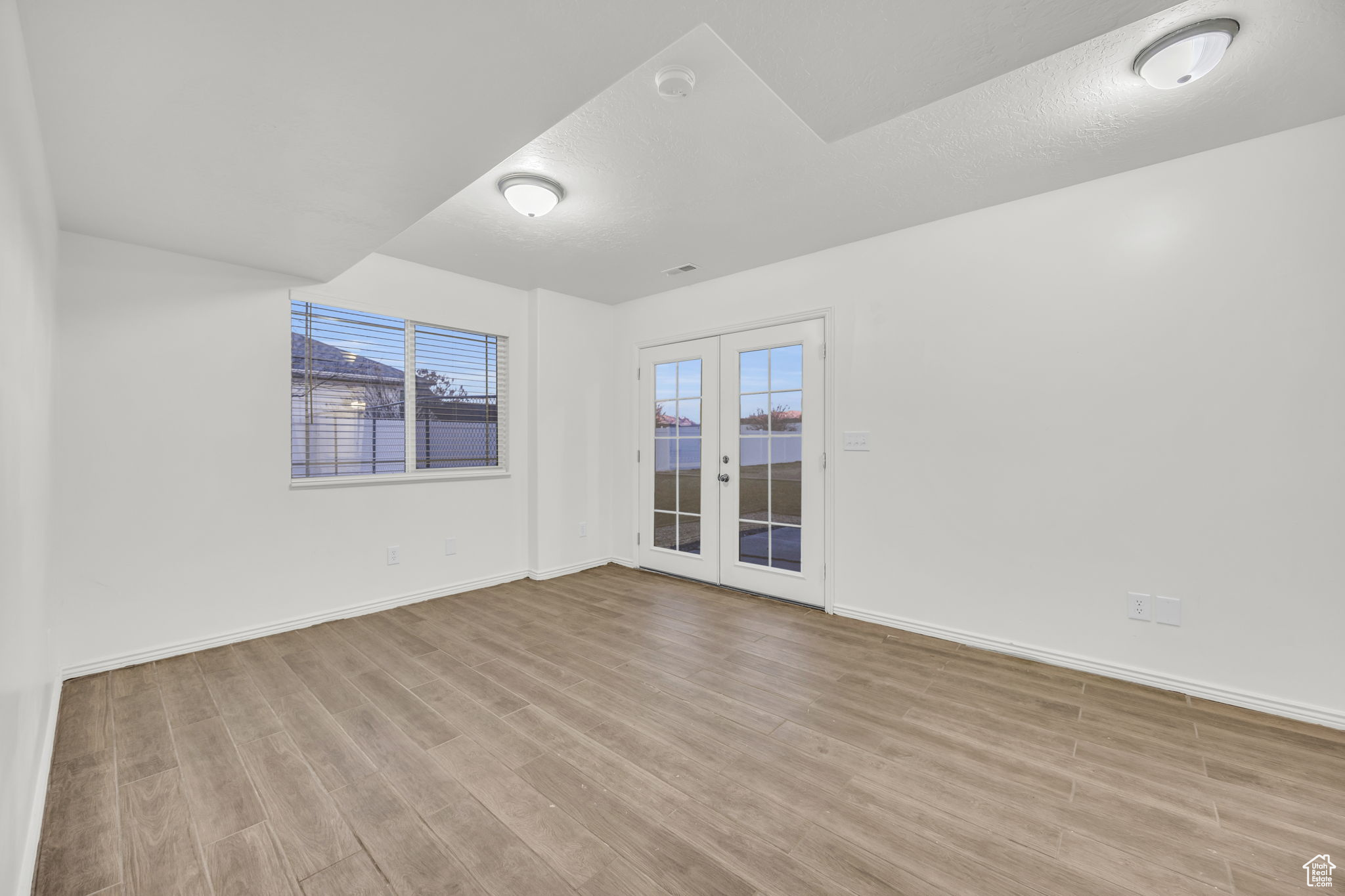 Empty room with french doors, a textured ceiling, and light hardwood / wood-style flooring