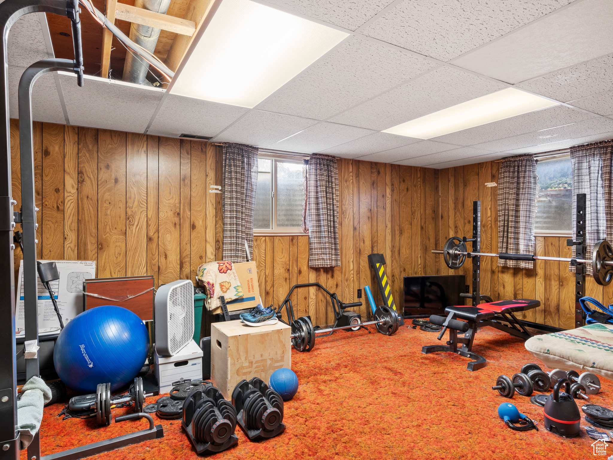 Exercise room featuring carpet flooring, a paneled ceiling, and wooden walls