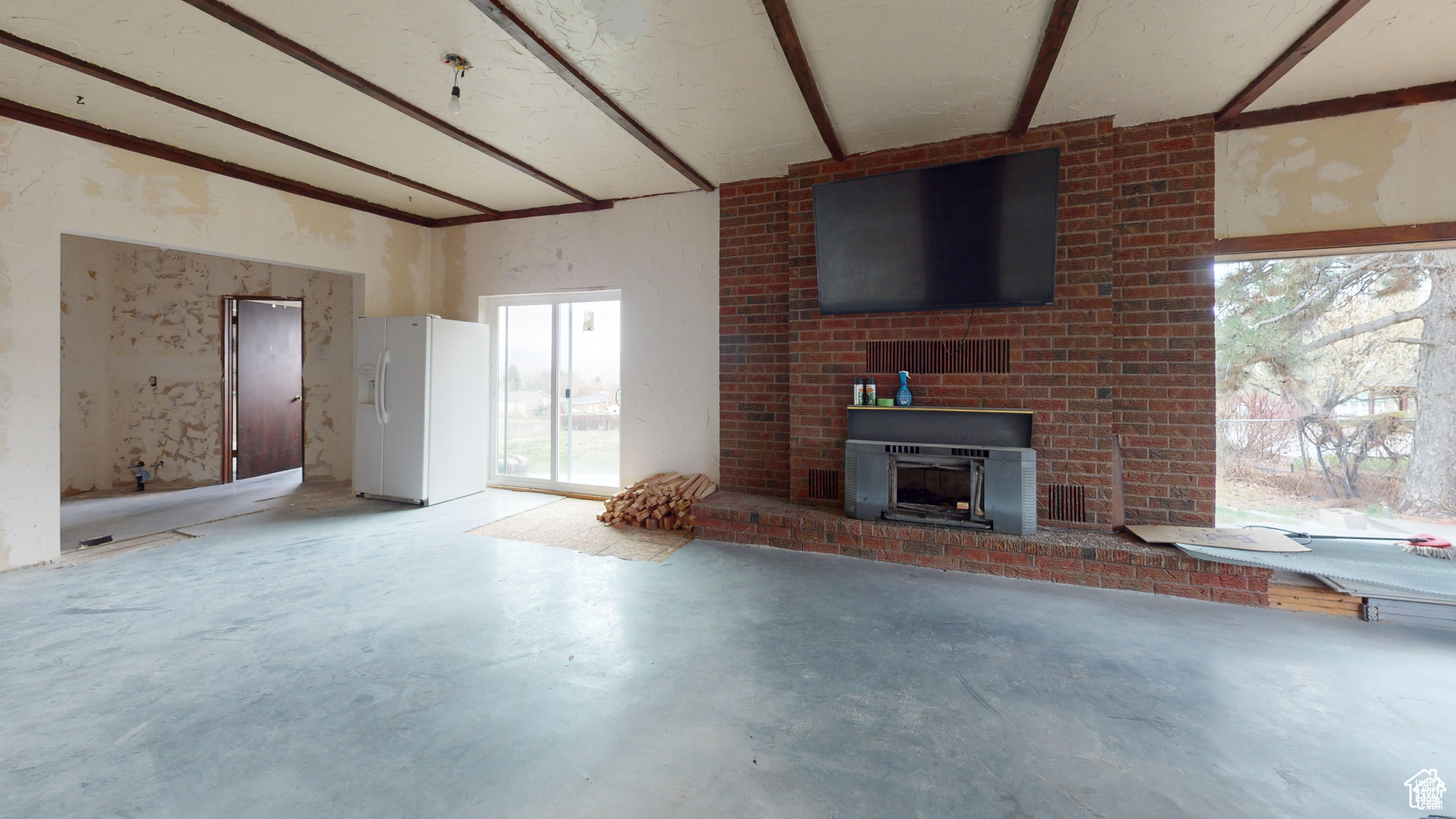 Unfurnished living room featuring concrete flooring, a wood stove, and beamed ceiling